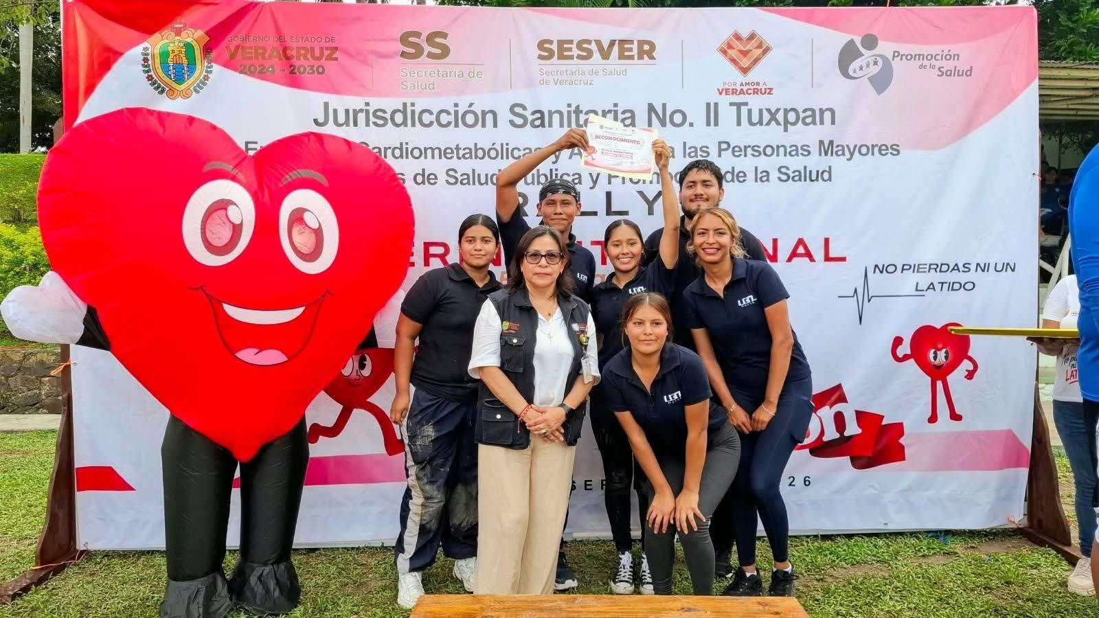 Equipo junto a la botarga de corazón frente a la lona del rally de la Jurisdicción Sanitaria No. II Tuxpan.
